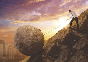 Picture of Caucasian businessman pulling a rock while climbing a cliff. Shot at sunrise time